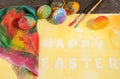 Easter colorful eggs with two painter brushes and a hand painted cloth,arranged on watercolor paper with yellow painted text. Royalty Free Stock Photo