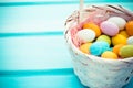 Easter colorful sweet eggs in white basket on turquoise wood background. Copyspace Royalty Free Stock Photo