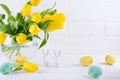 Easter composition with bouquet of yellow tulip flowers in glass vase and two white ceramic rabbits on white Royalty Free Stock Photo