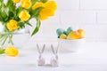 Easter composition with bouquet of yellow tulip flowers in glass vase and two white ceramic rabbits on white Royalty Free Stock Photo