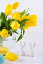 Easter composition with bouquet of yellow tulip flowers in glass vase and two white ceramic rabbits on white Royalty Free Stock Photo