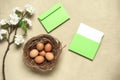 Easter composition. Brown eggs in the nest, cherry blossom branch artificial and mockup blank greeting card in an envelope.