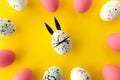 Easter composition with colored eggs and egg with bunny ears and face on yellow background