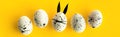 Easter composition with colored eggs and egg with bunny ears and face on yellow background
