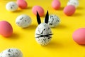 Easter composition with colored eggs and egg with bunny ears and face on yellow background