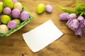 Easter composition with Easter eggs in basket purple tulips and message card on wood