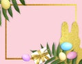 Easter composition with golden frame, colorful eggs,  glitter bunny cutout, green leaves on pink background. Royalty Free Stock Photo