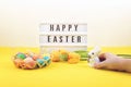 Easter composition, greeting card with child hand, toy bunny, lightbox text Happy Easter, colored decorative eggs, yellow tulips