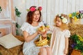 Easter composition. Mother and daughter in white dresses and flower wreaths on their heads play with ducklings. Farm village