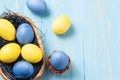 Easter composition - several colored eggs in a basket on a blue wooden table, place for text, copy space