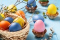 Easter composition - several colored eggs in a basket on a blue wooden table with willow twigs