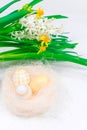 Easter concept. Close-up of yellow Easter eggs in a nest next to a bouquet of daffodils on a white concrete table. Place