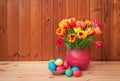 Easter concept. Colorful tulips in vase and Easter eggs in wicker basket on wooden table