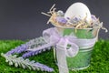 Easter concept - the egg in a decorative pail on the grass with Decker on a bright background