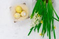 Easter concept. Yellow Easter eggs in a nest next to a bouquet of daffodils on a white concrete table. View from above
