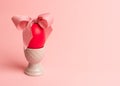 Easter creative concept. One red egg tied with a pink ribbon standinng in the egg cup a on a pink background. Minimalism, copy