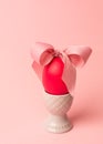Easter creative concept. One red egg tied with a pink ribbon standinng in the gray egg cup a on a pink background. Minimalism,