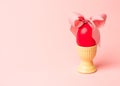 Easter creative concept. One red egg tied with a pink ribbon standinng in the yellow egg cup a on a pink background. Minimalism,