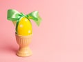 Easter creative concept. One yellow egg tied with a green ribbon standinng in the yellow egg cup a on a pink background.