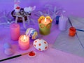 Easter decor, painted eggs, paints, brushes, lighted pink candles on a lilac background, preparation for the Easter holiday
