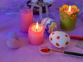 Easter decor, painted eggs, paints, brushes, lighted pink candles on a lilac background, preparation for the Easter holiday