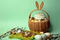 Easter decorations in a basket with rabbit ears. Easter cake and eggs on moss, quail eggs and feathers on mint green background. Royalty Free Stock Photo