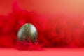 Easter egg in a beautiful dark green color with scratches and specks against a background of red feathers. Close-up. Horizontal Royalty Free Stock Photo