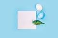 Easter egg hunt holiday composition, paper note or list with colorful eggs, dinosaur on light blue backgroind. Seasonal Royalty Free Stock Photo