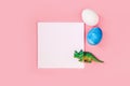 Easter egg hunt holiday composition, paper note or list with colorful eggs, dinosaur on light pastel pink backgroind Royalty Free Stock Photo