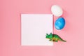 Easter egg hunt holiday composition, paper note or list with colorful eggs, dinosaur on light pastel pink backgroind Royalty Free Stock Photo