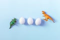 Easter egg hunt holiday composition, white eggs with coloful dinosaur on light pastel blue backgroind. Seasonal spring Royalty Free Stock Photo