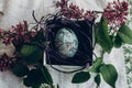 easter egg in nest with floral and chick ornaments on rustic background with lilac flowers. top view. space for text. happy Royalty Free Stock Photo