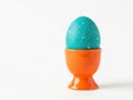 Easter Egg in Orange Egg Cup, Speckled Teal, White Background Royalty Free Stock Photo
