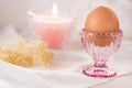 Easter egg in pink crystal cup,white linen cloth background,burning candle,bouquet of spring flowers Royalty Free Stock Photo