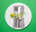 Easter egg in a white plate, gray napkin and cutlery, green color background, top view Royalty Free Stock Photo