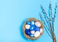 Easter eggs of blue flowers in a decorative nest of straw and pussy-willow branches on a blue background, copy space, flat lay Royalty Free Stock Photo