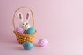 4 easter eggs and a bunny in small basket on pink background