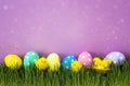Easter eggs with decorative chicken in fresh green grass on purple background. Royalty Free Stock Photo