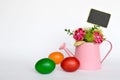 Easter eggs and fabric flowers arranged in watering bucket on light background