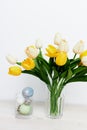 Easter eggs in a glass and yellow tulips in a vase on a light background Royalty Free Stock Photo