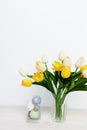 Easter eggs in a glass and yellow tulips in a vase on a light background Royalty Free Stock Photo