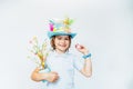 Easter eggs hunt tradition. Smiling boy kid in Easter hat holds easter tree in pot and chocolate egg in other hand on the white