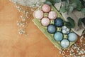 Easter eggs natural dye in carton tray on rustic table with flowers, flat lay. Modern pastel pink and blue easter eggs painted