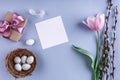 Easter eggs in nest and tulips flowers on blue background with card. Greeting card for Happy Easter. Flat lay, top view Royalty Free Stock Photo