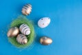 Easter eggs painted in gold colors in different patterns lie in a nest of green grass and next to it on a blue background. Easter Royalty Free Stock Photo