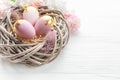 Easter eggs painted pink and gold and feathers in a nest on a white wooden background Royalty Free Stock Photo