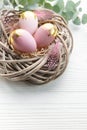 Easter eggs painted pink and gold and feathers in a nest on a white wooden background Royalty Free Stock Photo