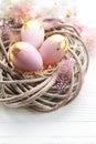 Easter eggs painted pink and gold and feathers in a nest on a white wooden background Royalty Free Stock Photo