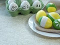 Easter eggs painted with yellow and green paint depicting flowers and stripes lie on a white plate. The container contains white