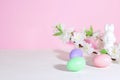 Easter eggs, pink, green and lilac, on a concrete white table, next to bunnie and flowers, on a pink background. Pastel shades